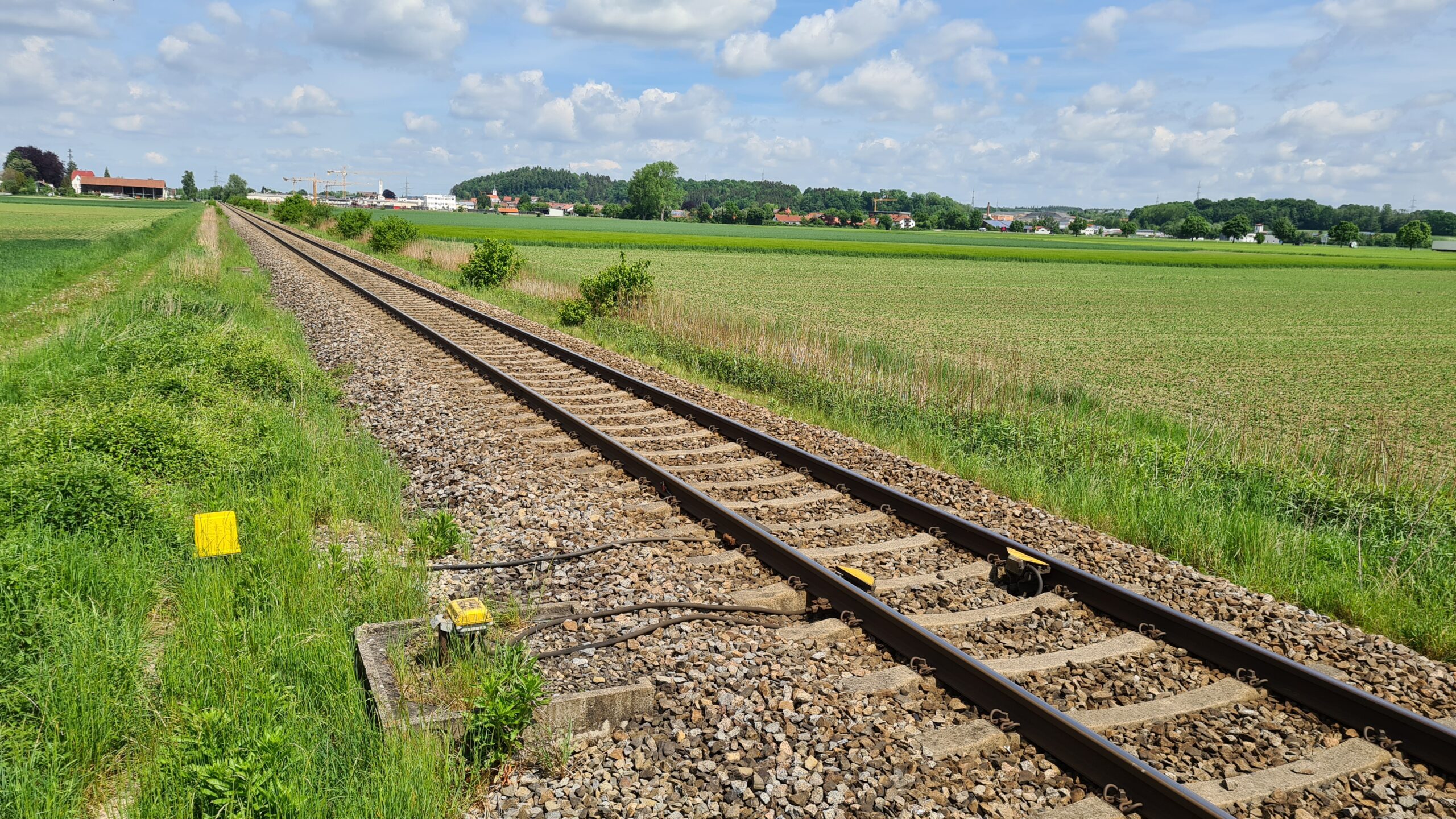 Eine eingleisige Strecke zwischen Feldern an einem sonnigen Tag.